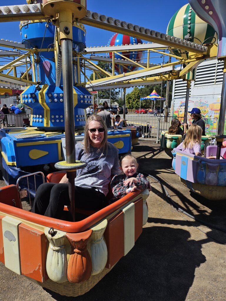 A toddler laughing on a carnival balloon ride during her first carnival.