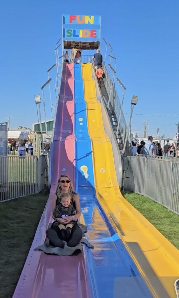 A toddler laughing on a carnival balloon ride during her first carnival.